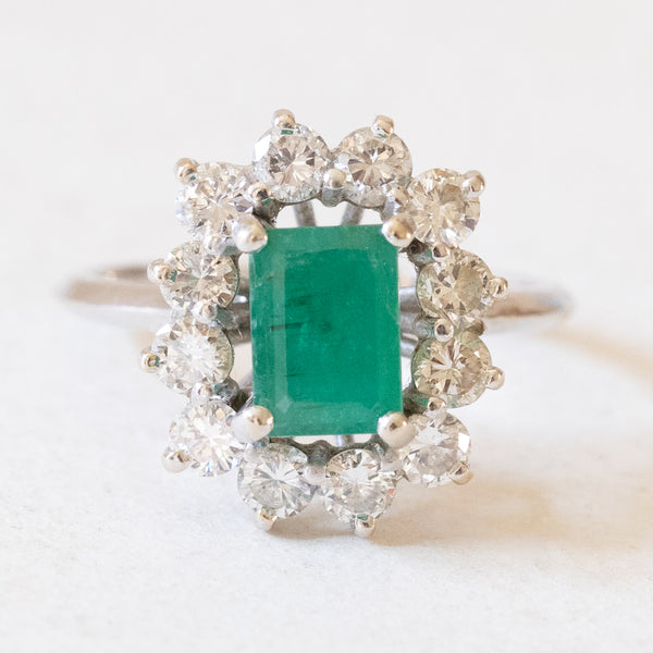 Anello vintage a margherita in oro bianco 18K con smeraldo (0.90ct ca.) e diamanti di taglio brillante (1.20ctw ca.), anni ‘60